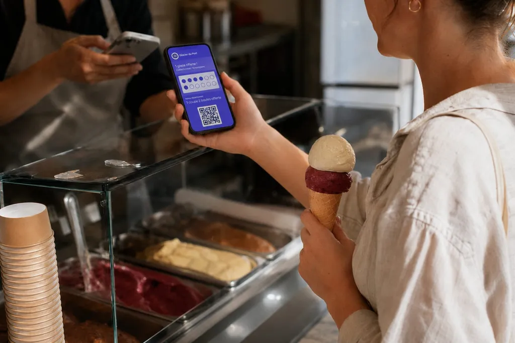 Carte de fidélité à tampons digitale sur un smartphone, présentée au comptoir d'un glacier pour être scannée
