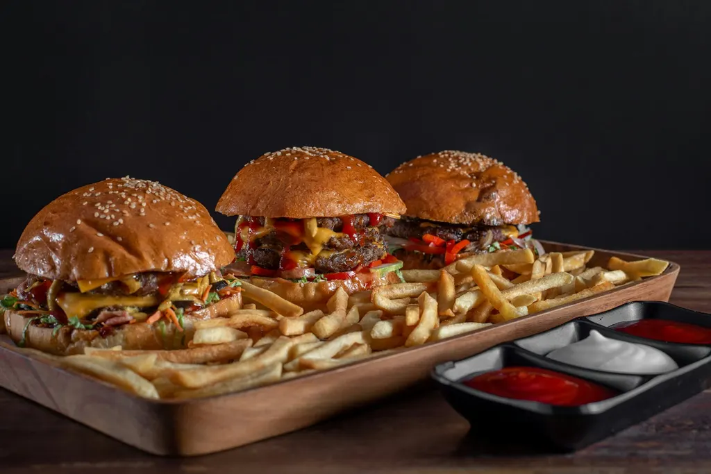 Trois burgers et des frites servis sur une planche, avec des sauces à côté